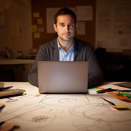 Portrait of Sumnesh Kutka in a creative workspace with a laptop and data sketches on the table